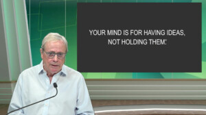 David Allen stands at a podium in front of a screen displaying, "Your mind is for having ideas, not holding them."