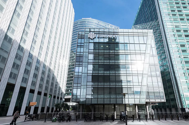 Modern glass building named Euronext amidst towering skyscrapers in an urban setting. Bicycles parked along the street, clear blue sky in background.