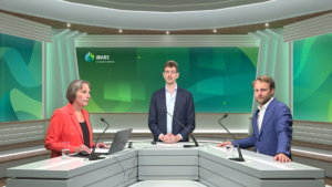 Three people standing at a modern indoor podium, discussing. Green backdrop displays "iBABS, A Euronext Company." Each holds microphones and glass of water.